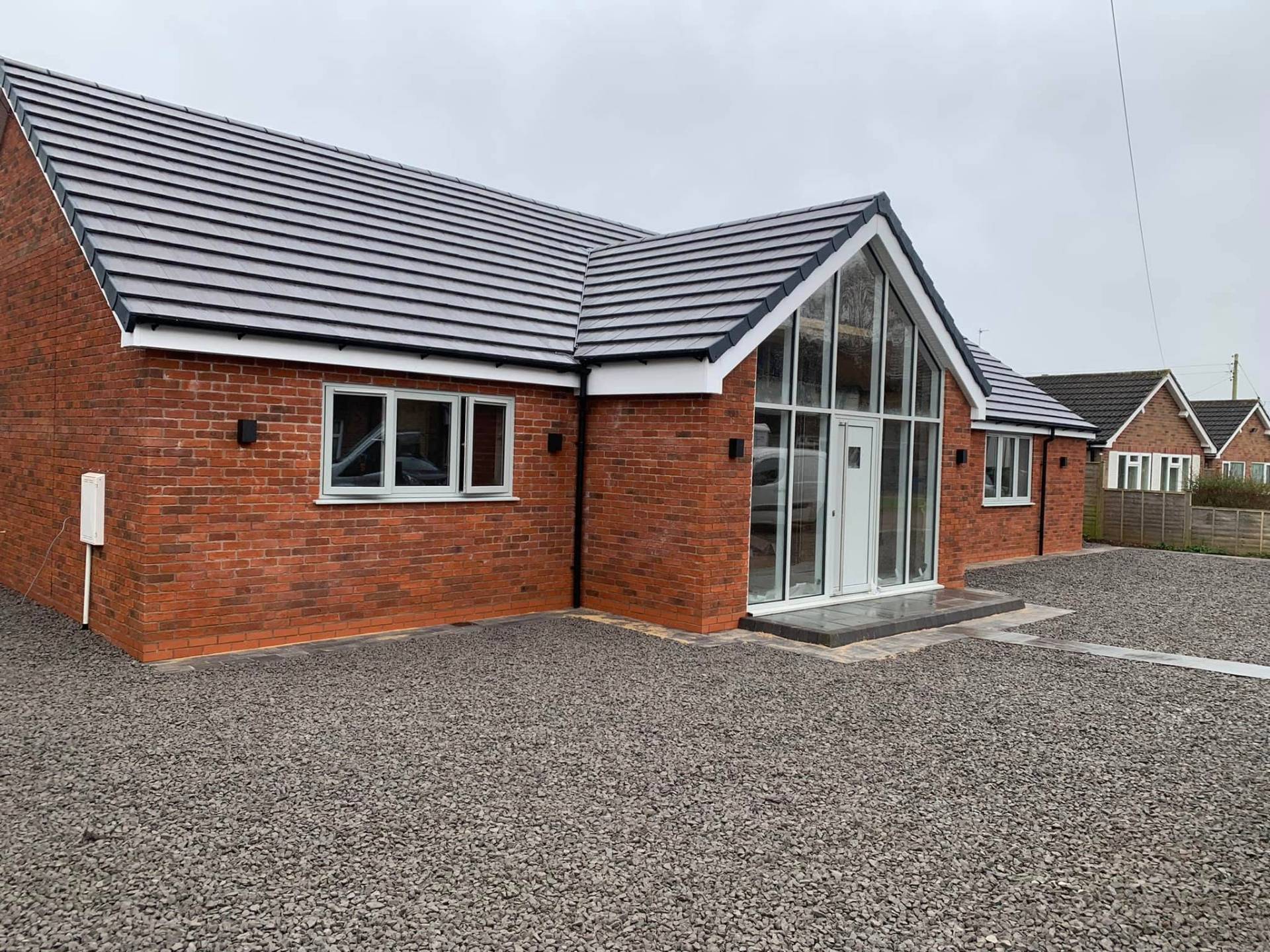 Finished front elevation of White Gates in Worcestershire, a tired two-bed bungalow transformed by JRC Developers into a modern three-bedroom home with red brick walls, grey plain tile roof and a full-height glazed gable entrance