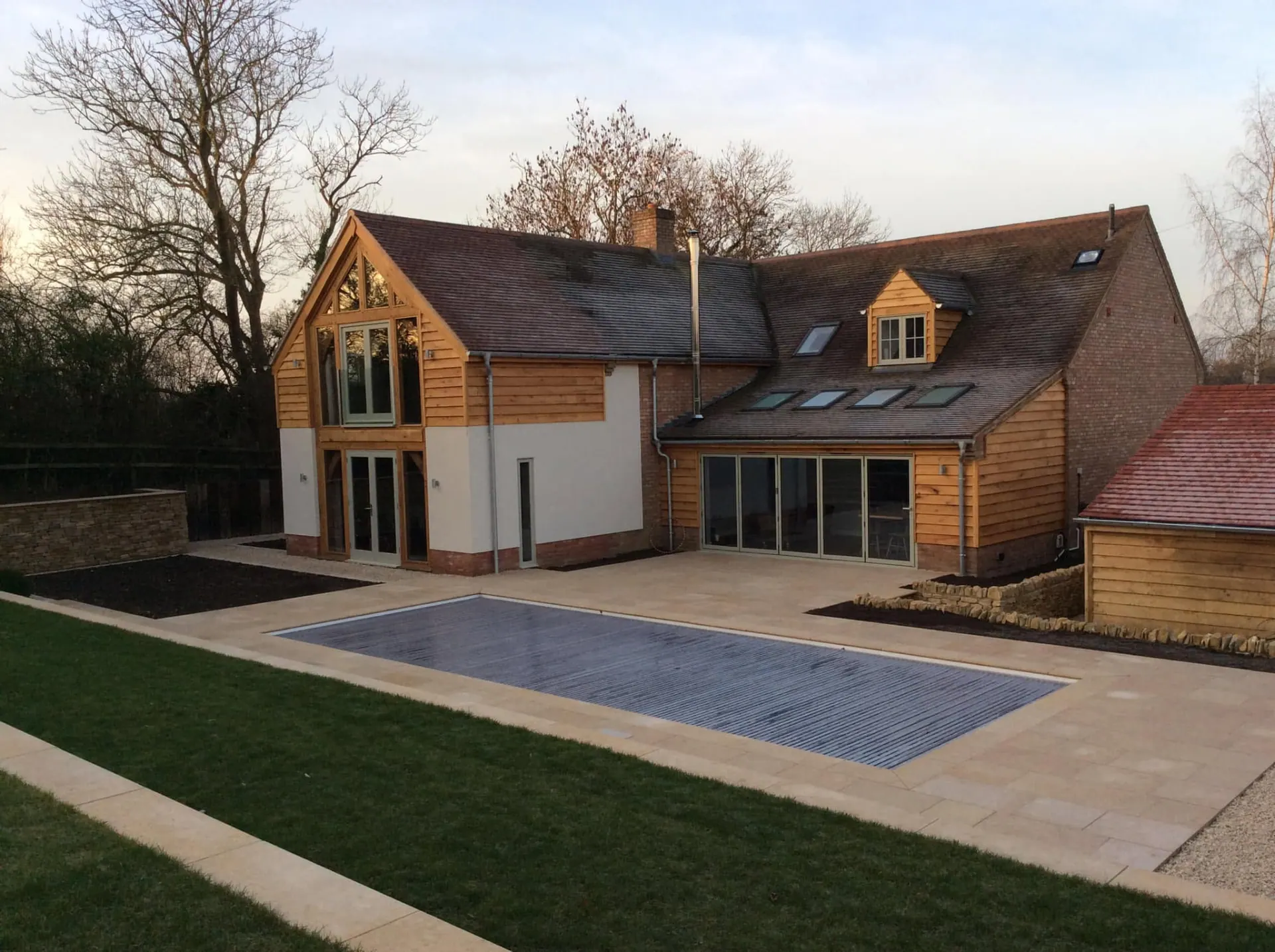 Willow House after remodelling by JRC Developers, oak-framed gables, oak weatherboard cladding and white render with a swimming pool and limestone terrace in the foreground