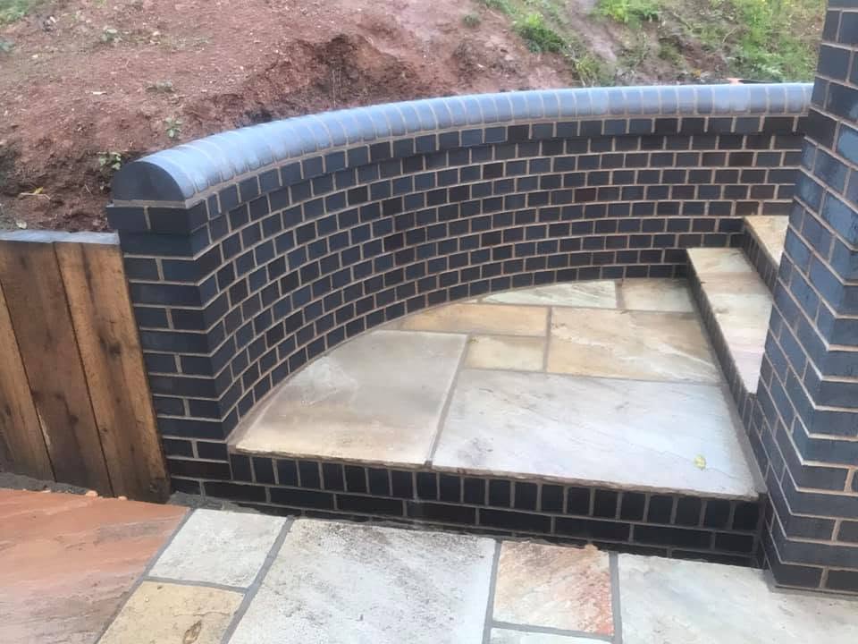 Curved blue brick retaining wall with bullnose coping beside a sandstone terrace, specialist brickwork by JRC Developers