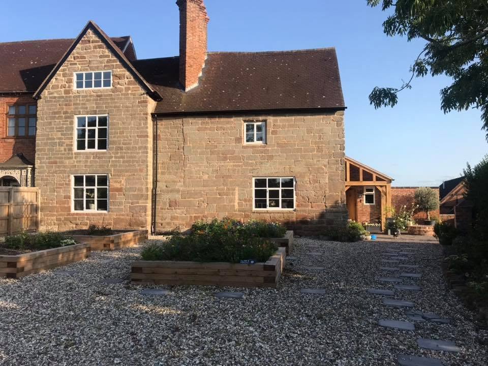 Restored Grade II listed sandstone farmhouse in Worcestershire with repointed stonework, new clay tiled roof, oak-framed porch, gravel courtyard and raised sleeper beds, restored by JRC Developers