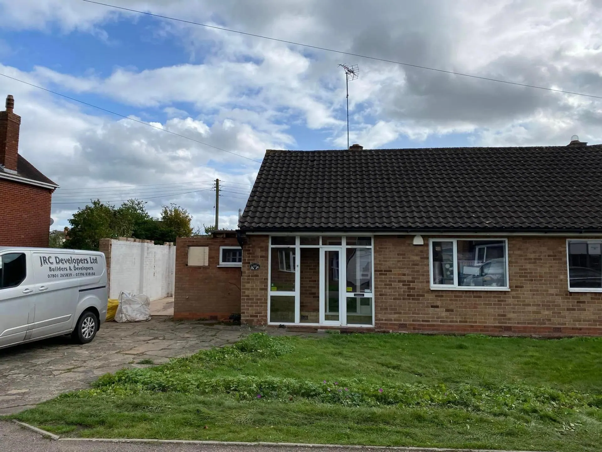 Original front elevation of the White Gates bungalow on day one with the JRC Developers Ltd van parked outside, dated brick porch, black concrete tile roof and tired garden