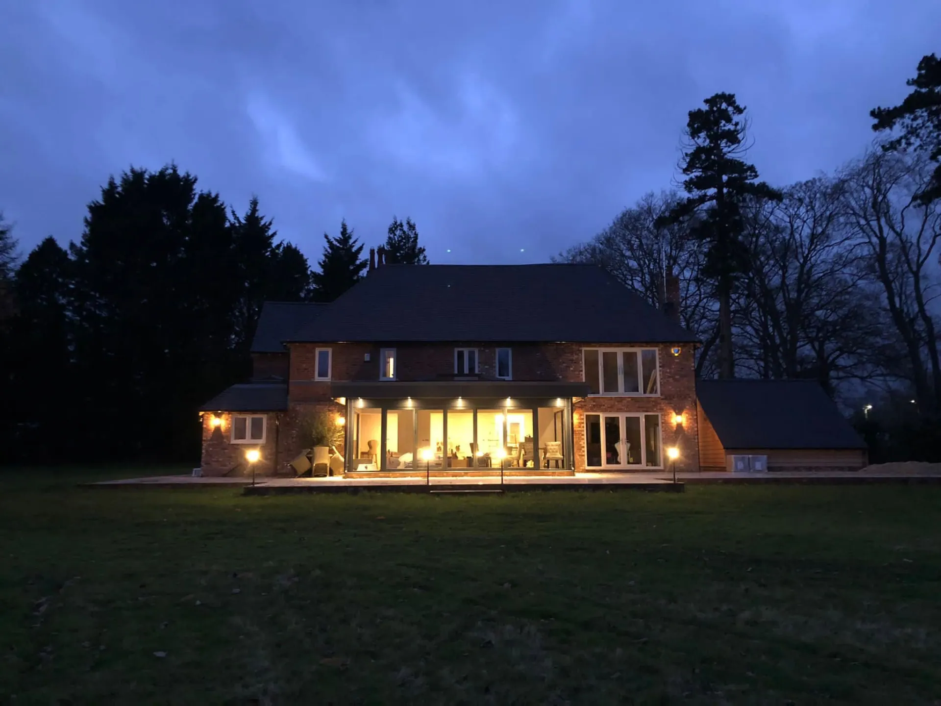 Rear elevation of Wootton Mead illuminated at night with the glazed garden room glowing from within